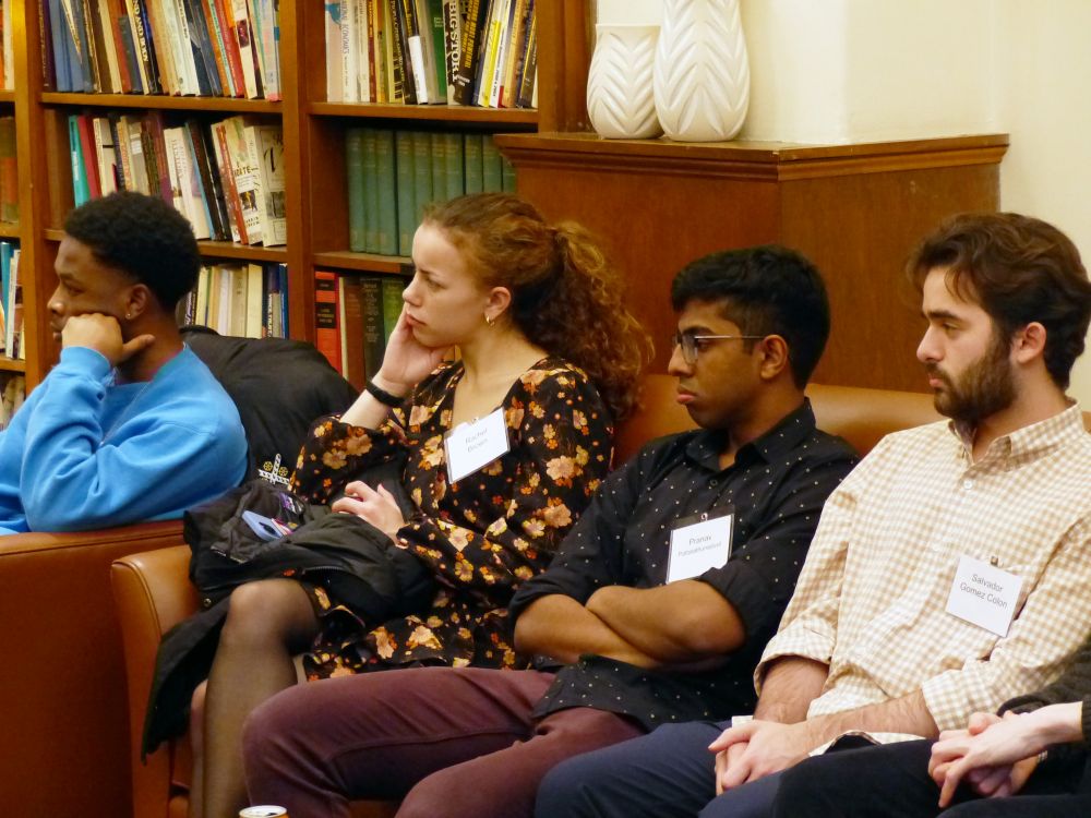 Four students sit in a library and listen to a speaker