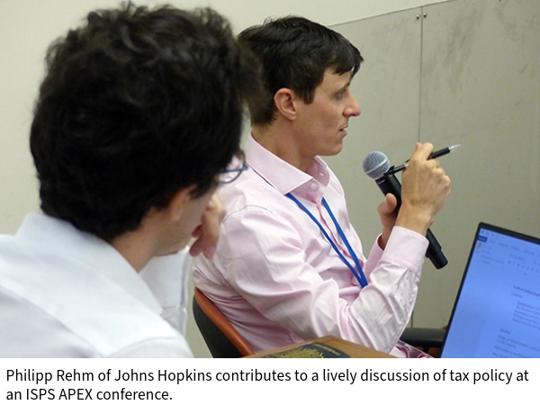 Phiipp Rehm of Johns Hopkins contributes to a lively discussion of tax policy at an ISPS APEX conference, seated, using a microphone as another participant looks on from behind