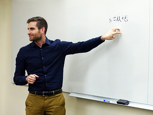 Joshua Kalla gestures to an equation on a whiteboard in a classroom