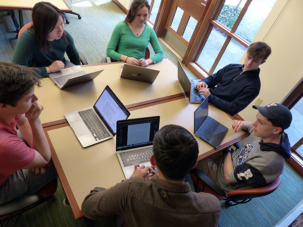 Students meet around a table with laptops out