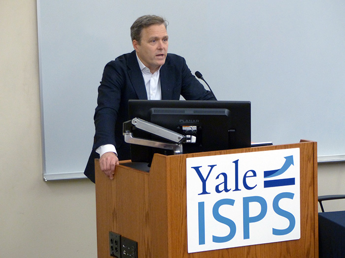 Nicholas Bagley speaks behind a lectern with the Yale ISPS logo in a classroom