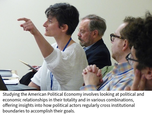A conference attendee questions a panelist as other members of the audience in a classroom look on.