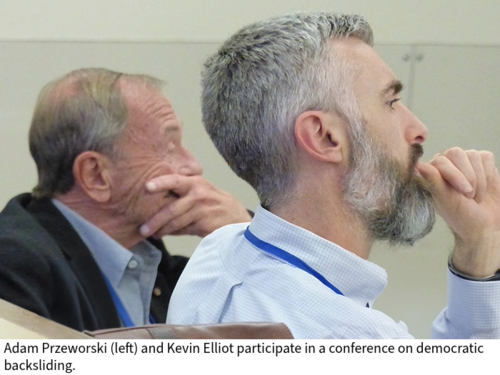 Adam Przeworksi and Kevin Elliot listen in the audience of a presentation in a classroom with their hands on their chins.