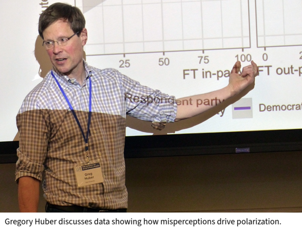 Gregory Huber speaks in front of a projection screen showing a chart