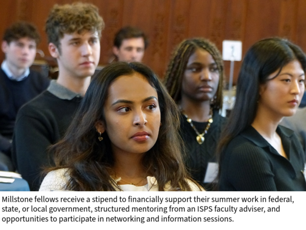 Students listen to a speaker, seated at tables in a wood-paneled room
