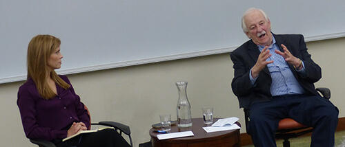 Bonnie Weir listens to Bruce Morrison speak as both are seated in the front of a classroom