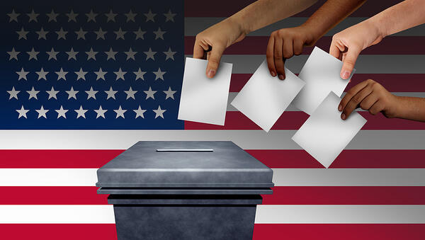 Four hands place votes into a box in front of an American flag