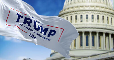Flag with Donald Trump 2024 presidential election campaign logo waving in front blurred US congress.
