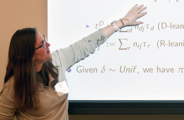 Allison Stashko gestures at a projection of scientific equations on a screen