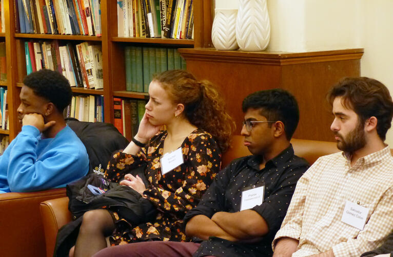 Four students listen to a speaker while seated in a library