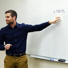 Joshua Kalla gestures to an equation on a whiteboard in a classroom