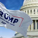 Flag with Donald Trump 2024 presidential election campaign logo waving in front blurred US Congress.