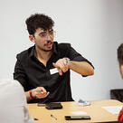 A student gestures while speaking to other students seated at a table.