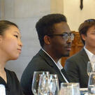 Students listen to a speaker while seated at a dining table covered in glasses