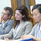 Three participants in a conference listen while seated at a table in a classroom